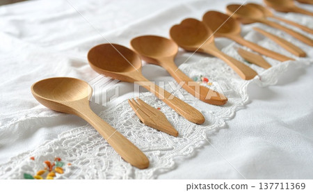 一把木湯匙和一把木叉擺放在一塊繡有精緻圖案的白色蕾絲布的邊緣。 137711369