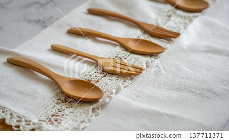 一把木湯匙和一把木叉擺放在一塊繡有精緻圖案的白色蕾絲布的邊緣。 137711371