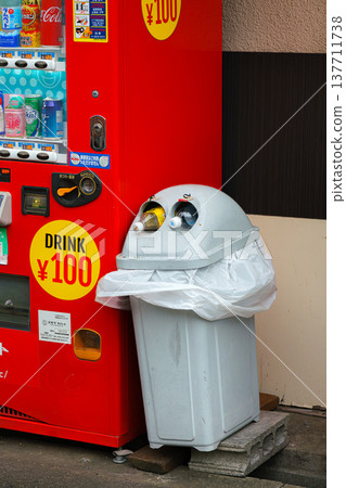 Osaka, Japan - Sep 21 2024, close up view of a trash can with beverage cans sticking out of it, there is a red vending machine next to it on the street at daytime, Osaka, Japan 137711738
