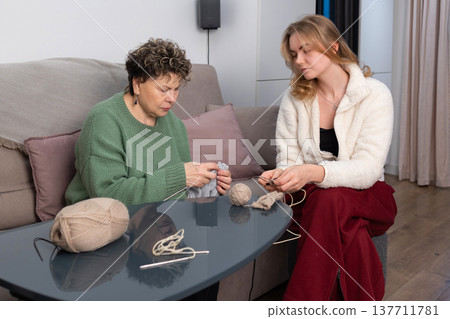 Mother and daughter knitting together at home on sofa Mother and daughter knitting together at home on sofa 137711781