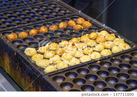 Osaka, Japan - Sep 21 2024, A close-up view of takoyaki cooking in a frying pan, a national Japanese dish in the form of fried balls with octopus, Osaka, Japan 137711800