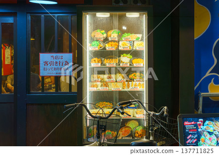 Osaka, Japan - Sep 21 2024, A close-up view of the glass showcase of a restaurant with wax models of Japanese cuisine, with a bicycle parked in foreground, without people, at evening, Osaka, Japan 137711825