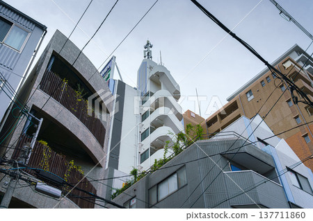 Osaka, Japan - Sep 21 2024, Panoramic view from the bottom up to the facade of various multi-storey apartment buildings, with grey cloudy sky and wires, at daytime, without people, Osaka, Japan 137711860