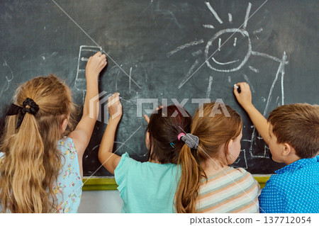 Four children drawing on a classroom chalkboard together, smiling and learning through play Four children drawing on a classroom chalkboard together, smiling and learning through play 137712054