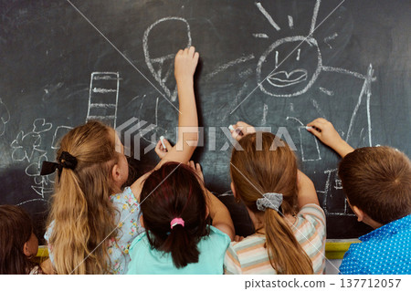 Children drawing together on a chalkboard in a playful elementary classroom activity Children drawing together on a chalkboard in a playful elementary classroom activity 137712057
