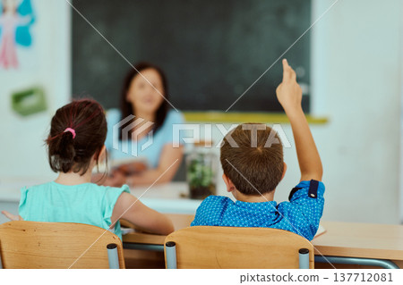 Student raising hand in classroom while teacher leads lesson with attentive classmates Student raising hand in classroom while teacher leads lesson with attentive classmates 137712081