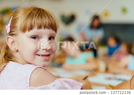 Smiling schoolgirl looking back in a colorful elementary classroom with classmates Smiling schoolgirl looking back in a colorful elementary classroom with classmates 137712136