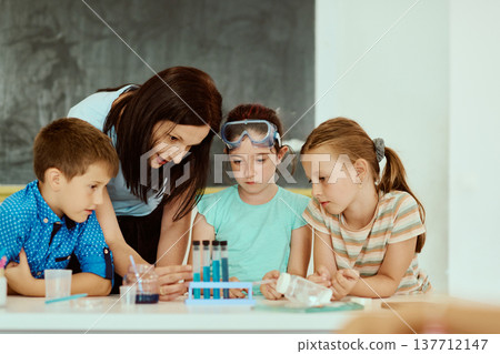 Teacher guiding children through a hands-on science experiment with test tubes in a classroom Teacher guiding children through a hands-on science experiment with test tubes in a classroom 137712147