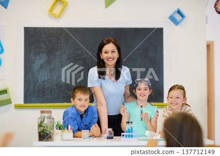 Teacher and elementary students smiling during a classroom science experiment with test tubes Teacher and elementary students smiling during a classroom science experiment with test tubes 137712149