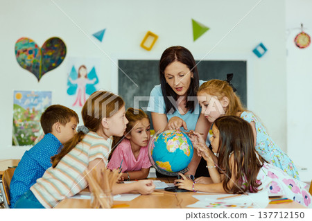 Teacher showing globe to curious elementary students gathered around a table in colorful classroom 137712150