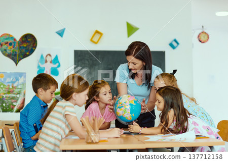 Teacher showing a globe to a group of curious children in a bright classroom learning together 137712158