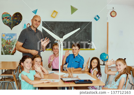 Teacher and elementary students in classroom with wind turbine model learning about renewable energy Teacher and elementary students in classroom with wind turbine model learning about renewable energy 137712163