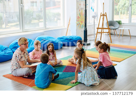 Preschool teacher reading to children during circle time in a bright classroom setting Preschool teacher reading to children during circle time in a bright classroom setting 137712179