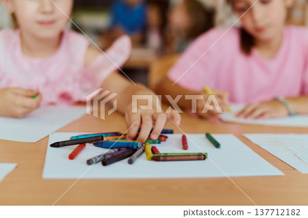 Children reaching for colorful crayons while drawing together at a classroom table 137712182