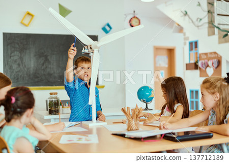Children in a classroom exploring a wind turbine model during a hands-on STEM science lesson 137712189