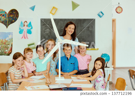 Teacher and elementary students smiling around a wind turbine model during a classroom science project Teacher and elementary students smiling around a wind turbine model during a classroom science project 137712196