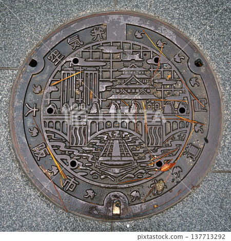 Osaka, Japan - Sep 22 2024, close-up view of a metal manhole with patterns depicting a bridge over a river, buildings and a pagoda, at Dotonbori district, Osaka, Japan Osaka, Japan - Sep 22 2024, close-up view of a metal manhole with patterns depicting a bridge over a river, buildings and a pagoda, at Dotonbori district, Osaka, Japan 137713292