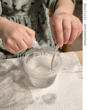 A girl mixes a solution in a plastic cup with a spoon. A girl mixes a solution in a plastic cup with a spoon. 137713509
