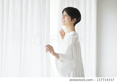 一位年輕女子像往常一樣拉開窗簾，沐浴在晨光中。 137714337