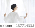 一位年輕女子像往常一樣生活，她拉開窗簾，在窗邊放鬆。 137714338