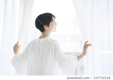 A young woman going about her daily life, opening the curtains and relaxing by the window. 137714338