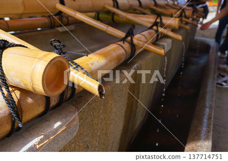 Kyoto, Japan - Sep 23 2024, close-up view Tsukubai stone bathtub with bamboo pipes through which water flows, at background people wash their hands, at entrance to Fushimi Inari shrine, Kyoto, Japan Kyoto, Japan - Sep 23 2024, close-up view Tsukubai stone bathtub with bamboo pipes through which water flows, at background people wash their hands, at entrance to Fushimi Inari shrine, Kyoto, Japan 137714751