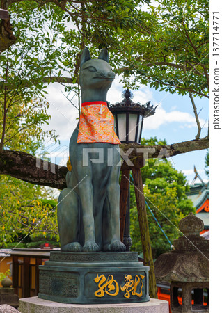 Kyoto, Japan - Sep 23 2024, Close-up view of the stone statue of kitsune, a Japanese fox holding a golden object in its mouth, with red facade of Fushimi-Inari Temple in background, Kyoto, Japan Kyoto, Japan - Sep 23 2024, Close-up view of the stone statue of kitsune, a Japanese fox holding a golden object in its mouth, with red facade of Fushimi-Inari Temple in background, Kyoto, Japan 137714771