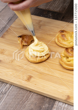 特寫鏡頭展現了廚房裡製作泡芙的手:將奶油餡擠入泡芙麵團中,並撒上糖粉。 特寫鏡頭展現了廚房裡製作泡芙的手:將奶油餡擠入泡芙麵團中,並撒上糖粉。 137715000