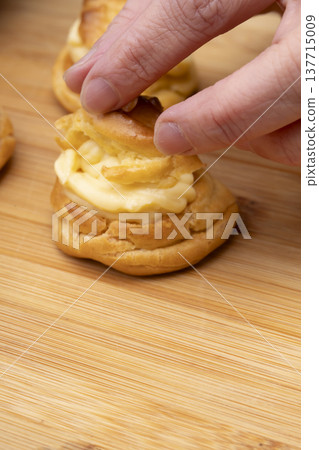 特寫鏡頭展現了廚房裡製作泡芙的手:將奶油餡擠入泡芙麵團中,並撒上糖粉。 特寫鏡頭展現了廚房裡製作泡芙的手:將奶油餡擠入泡芙麵團中,並撒上糖粉。 137715009