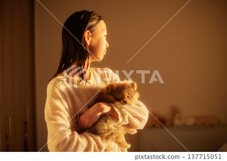 A cute middle school girl basking in the morning sunlight in her bedroom, holding a puppy. 137715051