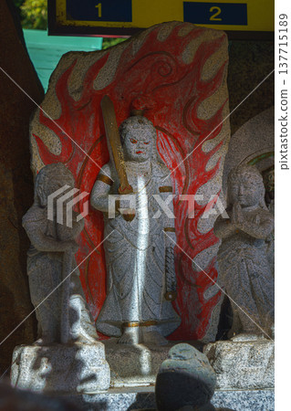 Kyoto, Japan - Sep 23 2024, A close-up view of the idol of god Fudo-meo, Acala, a stone statue wreathed in red flames, an altar on territory of the Fushimi Inari Temple, without people, Kyoto, Japan Kyoto, Japan - Sep 23 2024, A close-up view of the idol of god Fudo-meo, Acala, a stone statue wreathed in red flames, an altar on territory of the Fushimi Inari Temple, without people, Kyoto, Japan 137715189