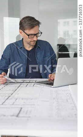 Architect man designing new building structure, carefully developing a modern architectural model in office, focusing on creating innovative housing plans and contemporary development concepts 137716353