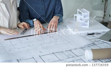 Architects working together, developing a building design by assembling a scale model and reviewing detailed blueprints, symbolizing teamwork, planning, and architectural creation 137716359