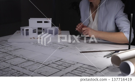 Architect analyzing blueprints and architectural scale model, planning a modern house construction project. Business and architect people concept 137716419
