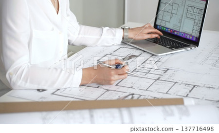 Architect working on building blueprint plans, designing new residential or commercial real estate projects for construction, using a ruler and laptop on a desk 137716498