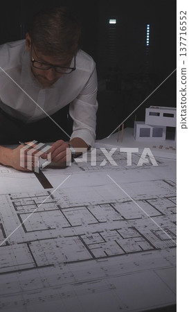 Professional architect working late, drawing blueprints for a new residential construction project. Concept of architecture, planning, and business in low-key lighting 137716552