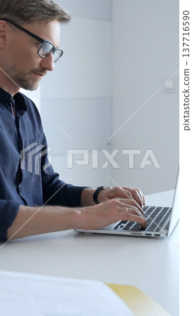 Professional businessman typing on laptop, surrounded by financial reports and digital tablet, working in contemporary corporate workspace. Business people concept Professional businessman typing on laptop, surrounded by financial reports and digital tablet, working in contemporary corporate workspace. Business people concept 137716590