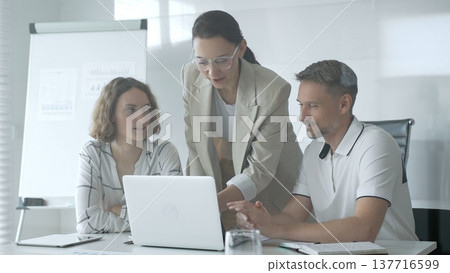 Business team collaborating and analyzing data on a laptop during a dynamic office meeting, uniting efforts to reach shared objectives and drive successful outcomes together 137716599