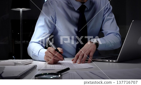 Businessman working overtime in office signing document at night, preparing contracts and finances. Audit and taxes in business Businessman working overtime in office signing document at night, preparing contracts and finances. Audit and taxes in business 137716707