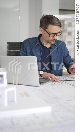 Architect man designing new building structure, carefully developing a modern architectural model in office, focusing on creating innovative housing plans and contemporary development concepts 137716797