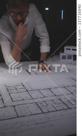 Architect drawing floor plans and looking at a house model, developing construction projects and residential building designs. Concept of architecture and business in low key lighting Architect drawing floor plans and looking at a house model, developing construction projects and residential building designs. Concept of architecture and business in low key lighting 137716840