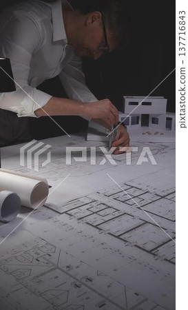 Professional architect working late, drawing blueprints for a new residential construction project. Concept of architecture, planning, and business in low-key lighting Professional architect working late, drawing blueprints for a new residential construction project. Concept of architecture, planning, and business in low-key lighting 137716843
