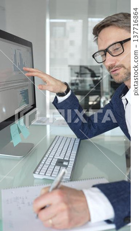 Professional businessman in a blue jacket working on desktop computer in modern office, focusing on his work and business tasks. Business people concept Professional businessman in a blue jacket working on desktop computer in modern office, focusing on his work and business tasks. Business people concept 137716864