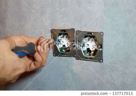 A worker installs an electrical outlet into a wall using a screwdriver A worker installs an electrical outlet into a wall using a screwdriver 137717013