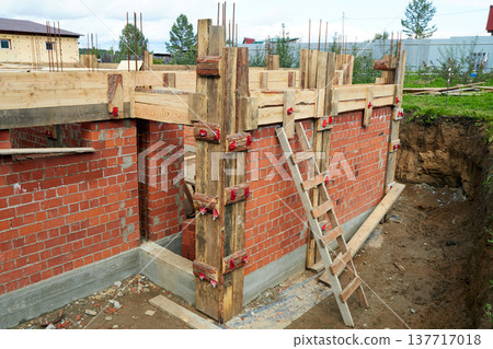 Brick walls are rising at a construction site, supported by wooden forms and metal rods. 137717018