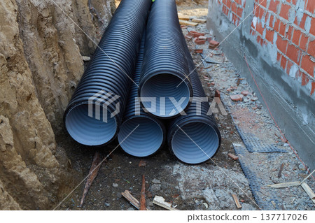 Workers are concentrated at a construction site where several black pipes are stacked on the ground. 137717026