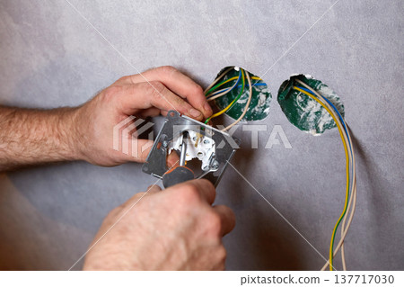 A worker installs an electrical outlet into a wall using a screwdriver A worker installs an electrical outlet into a wall using a screwdriver 137717030