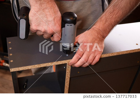 Person uses a power drill to assemble furniture in a room during daylight hours in a home setting 137717033