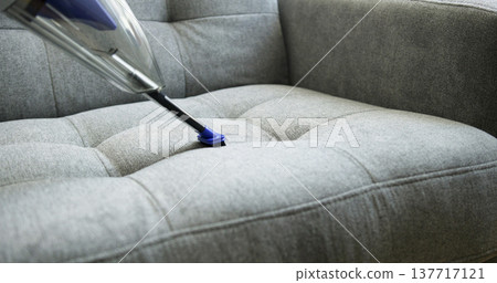 Cleaning a gray couch with a vacuum in a living room during the day Cleaning a gray couch with a vacuum in a living room during the day 137717121