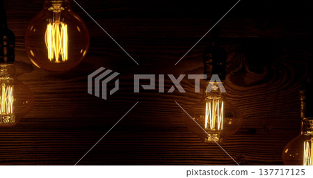 Warm light bulbs hang against a dark wood backdrop creating a cozy atmosphere for an indoor setting during an evening gathering 137717125